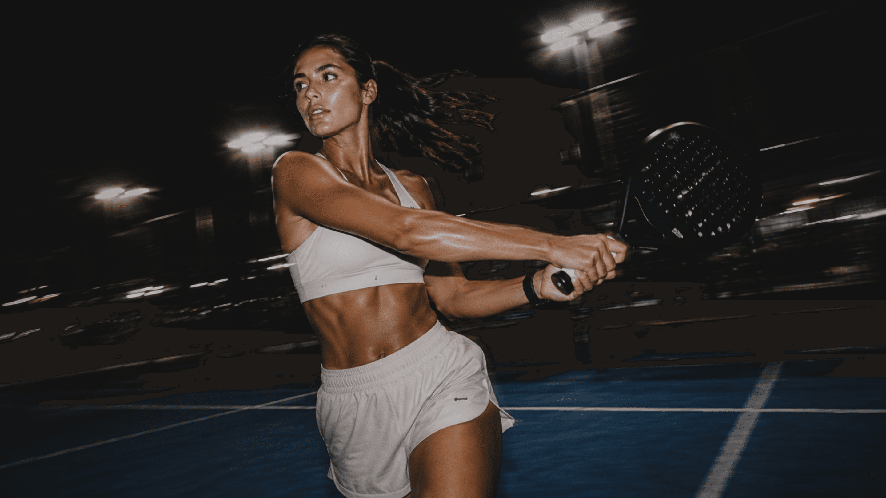 Padel player in action on a floodlit court at night